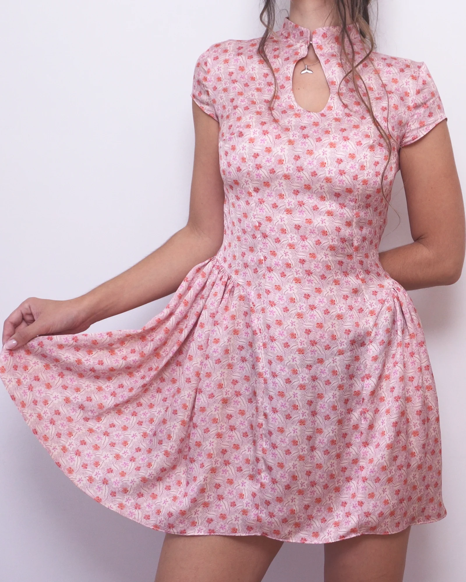 Model holding out the pink floral Ayris mini dress skirt to show its gathered side panels and volume.